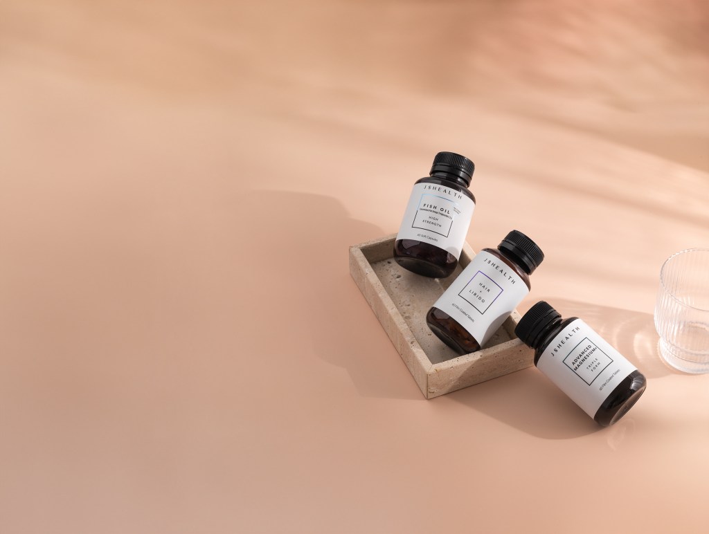 JS Health Vitamins bottles next to a glass of water including Hormone + Balance for endometriosis support and Advanced Magnesium+